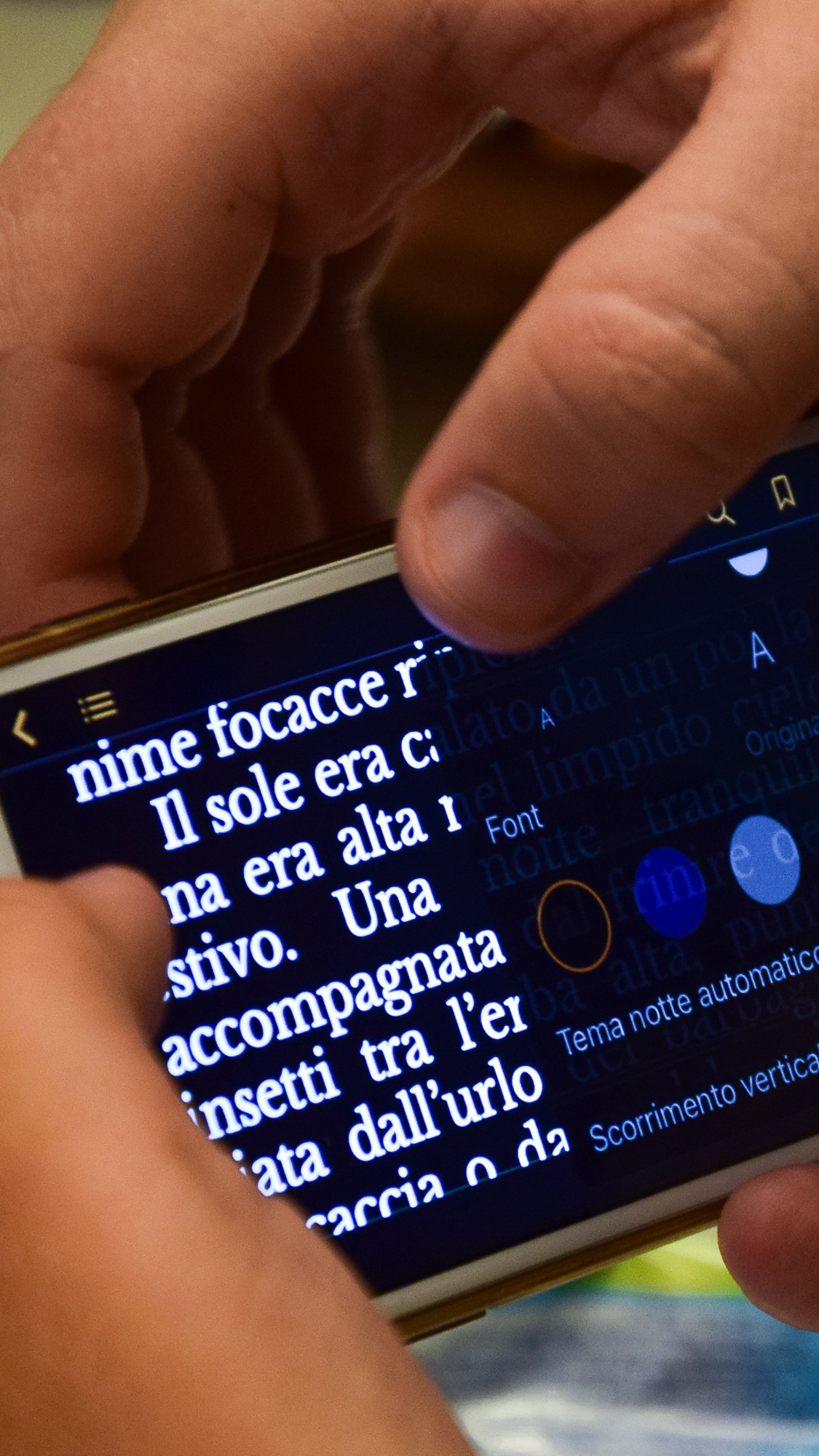 Fotografia di mani che usano smartphone. In primo piano sullo schermo un testo e le opzioni per personalizzare la visualizzazione