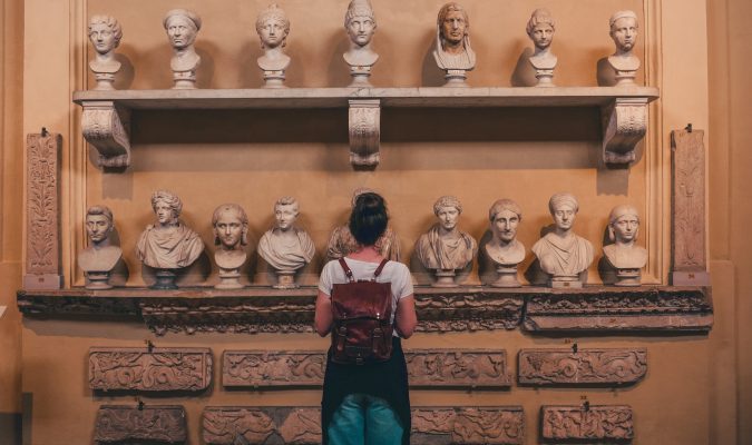 Fotografia di una ragazza di spalle di fronte a dei busti marmorei