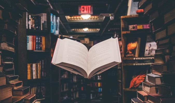 Photo of an open book surrounded by bookshelves