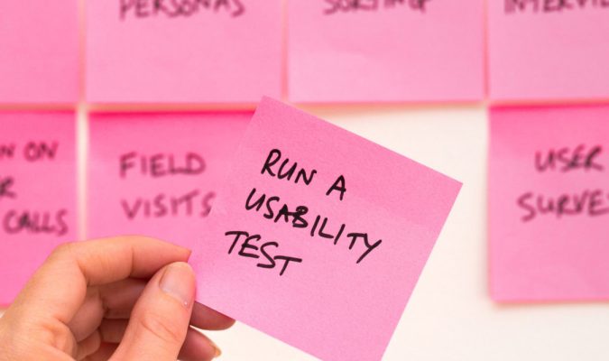 Fotografia di una mano che regge un post-it con la scritta run a usability test