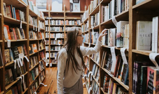 Fotografia di una ragazza che consulta dei libri su uno scaffale