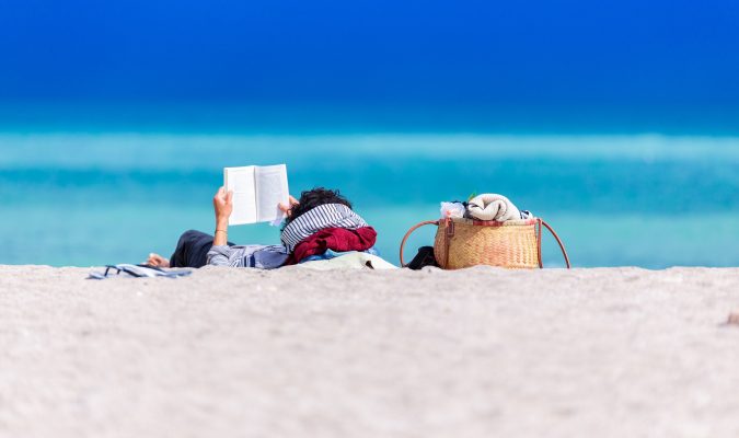 photo of a man reading a book by the sea