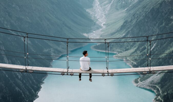 Fotografia di un uomo seduto su un ponte sospeso nel vuoto