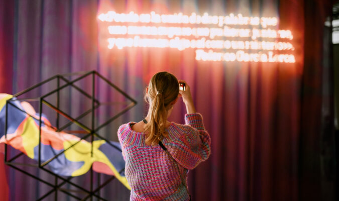 Fotografia di una persone di spalle che sta fotografando un muro con una scritta luminosa