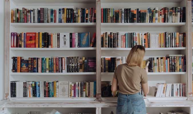Fotografia di una persona che consulta dei libri dallo scaffale di una libreria
